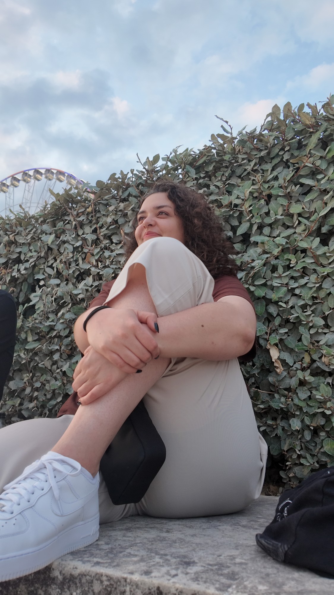 Esther (povbyzen) sitting in front of a hedge with a ferris wheel behind